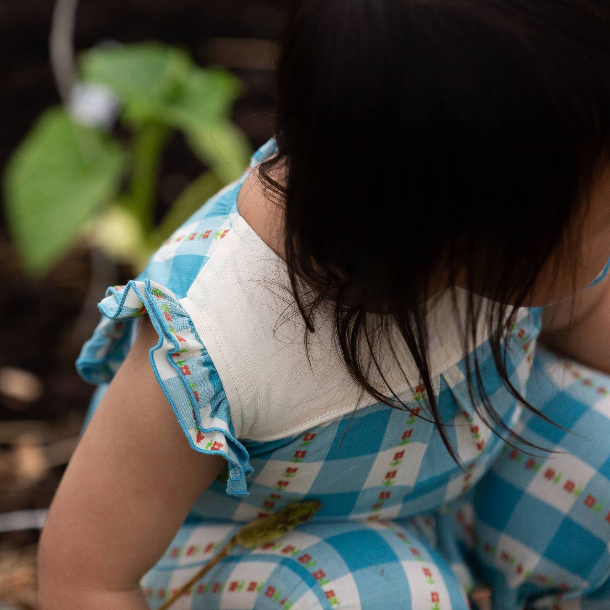 Child wearing a blue checkered dress with a white collar, sitting outdoors.