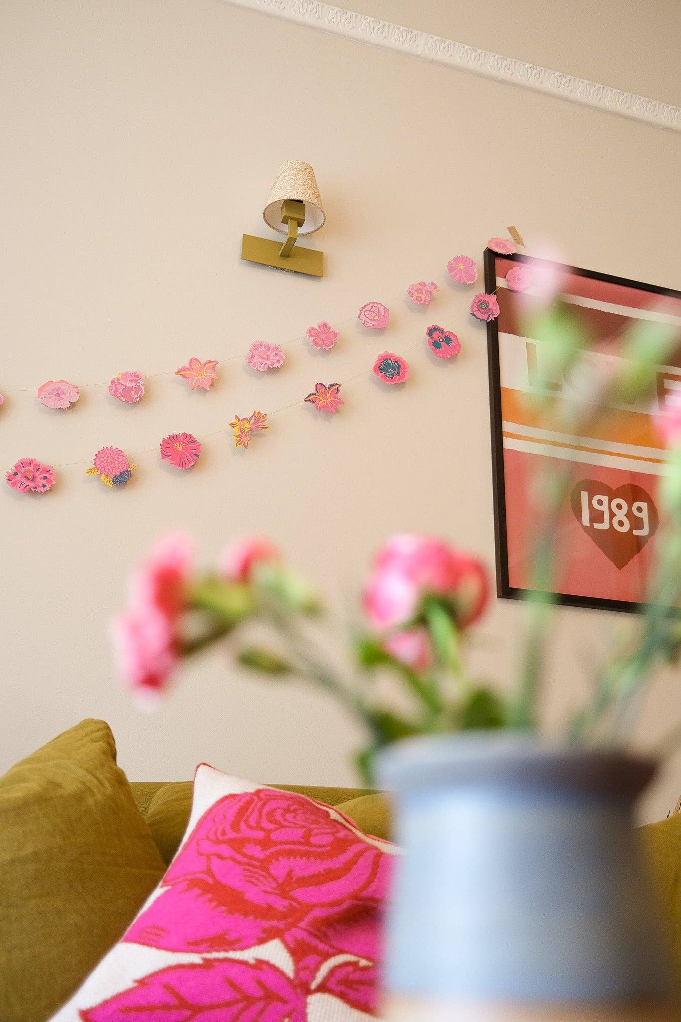 Decorative floral wall garland on a beige wall with a couch and floral arrangement in the foreground.