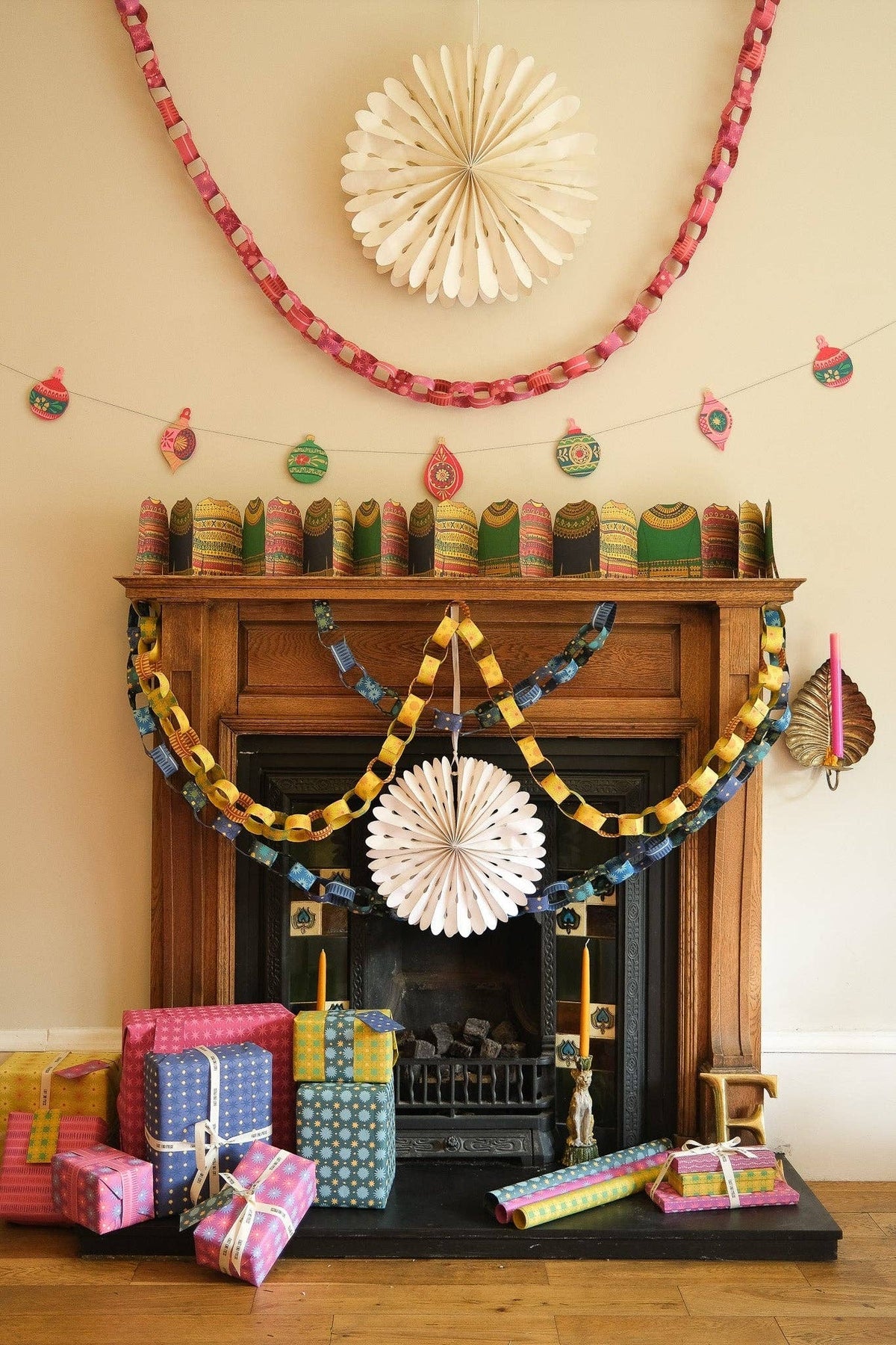 Fireplace decorated with yellow, blue and pink paper chains, white rosettes and wrapped gifts.