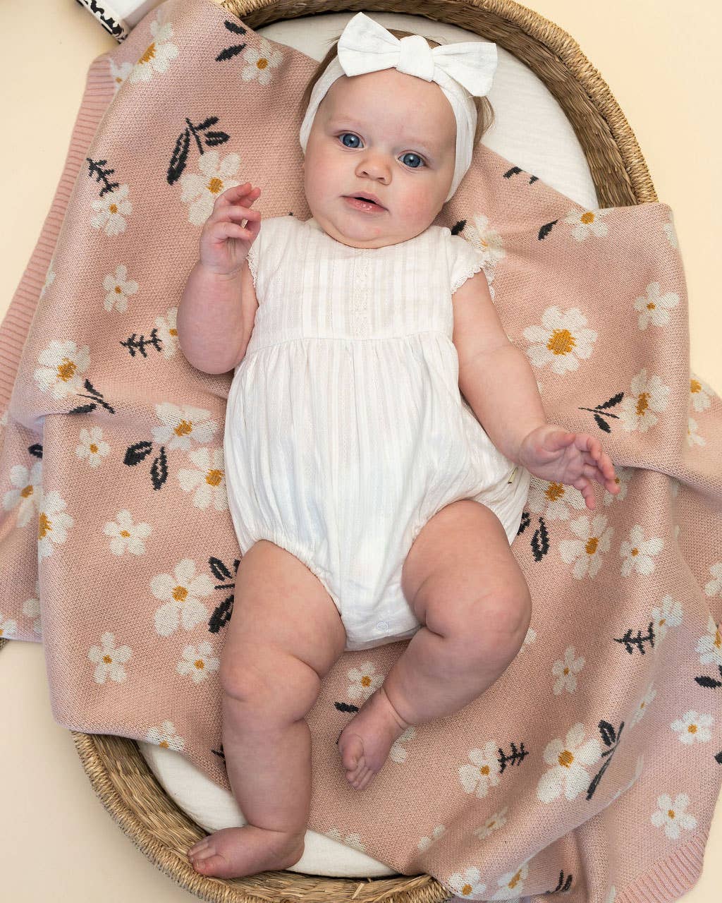 Baby in a white romper lying on a floral blanket