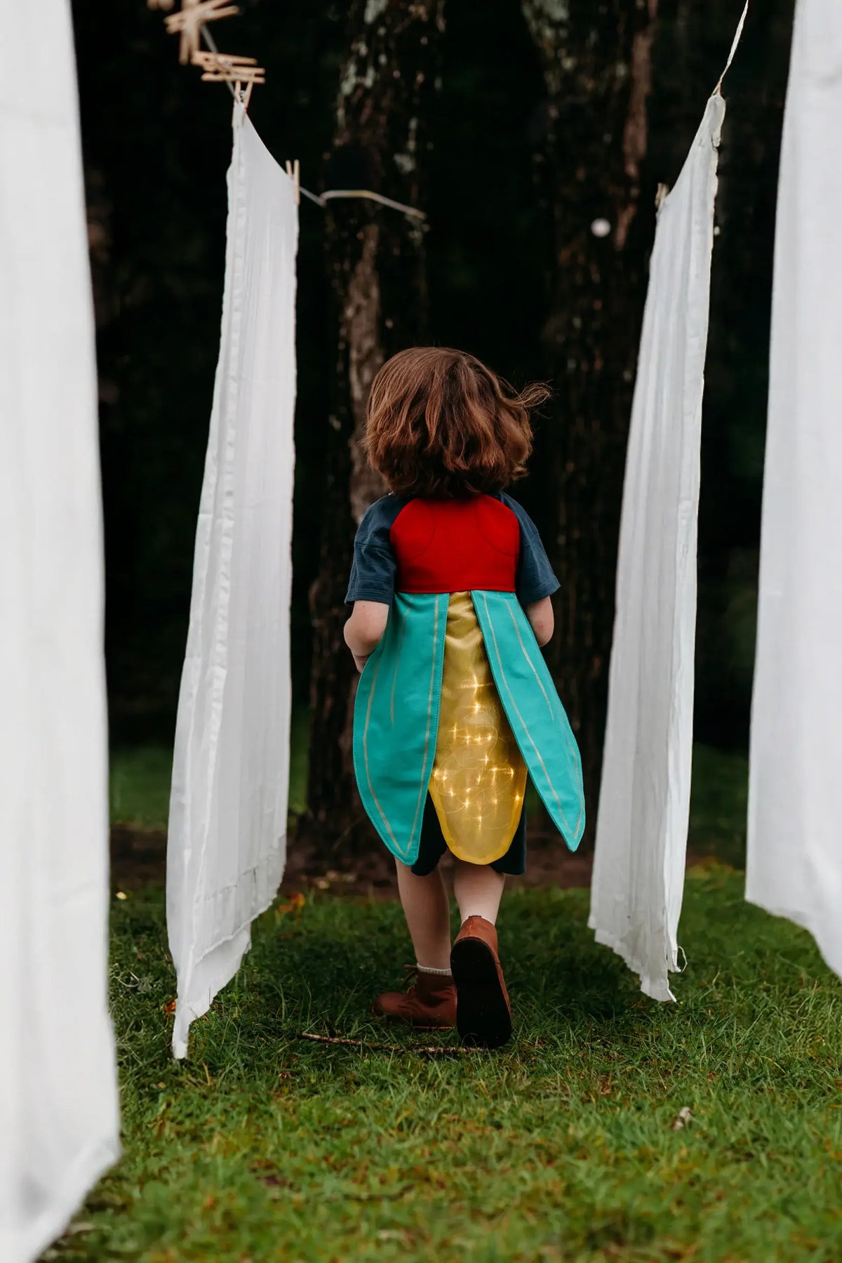 Child in a colorful costume standing between white curtains outdoors