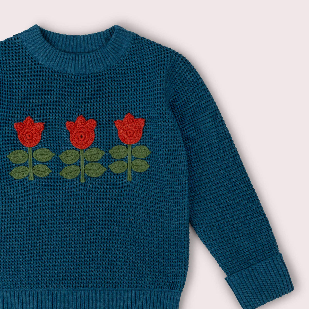Close-up of the ribbed neckline and red tulip decorations on a teal knitted jumper.