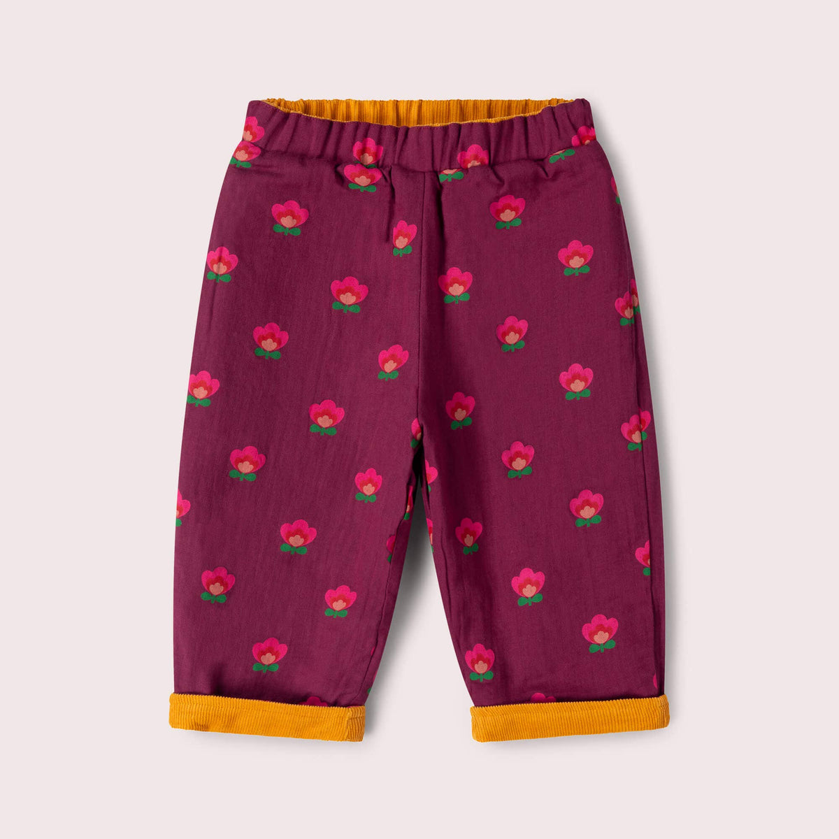 Purple pull-on trousers with pink flowers and turned-up cuffs showing mustard corduroy on the reverse.