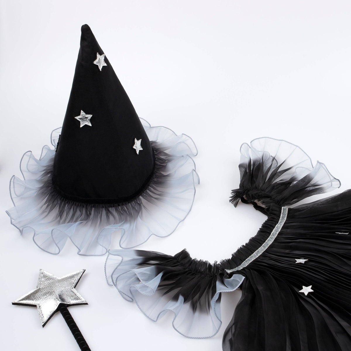 Black witch costume accessory set including a pointed hat with silver star embellishments and a ruffled black tulle trim, a matching black tulle skirt piece with a silver band, and a silver star wand, arranged on a white background.