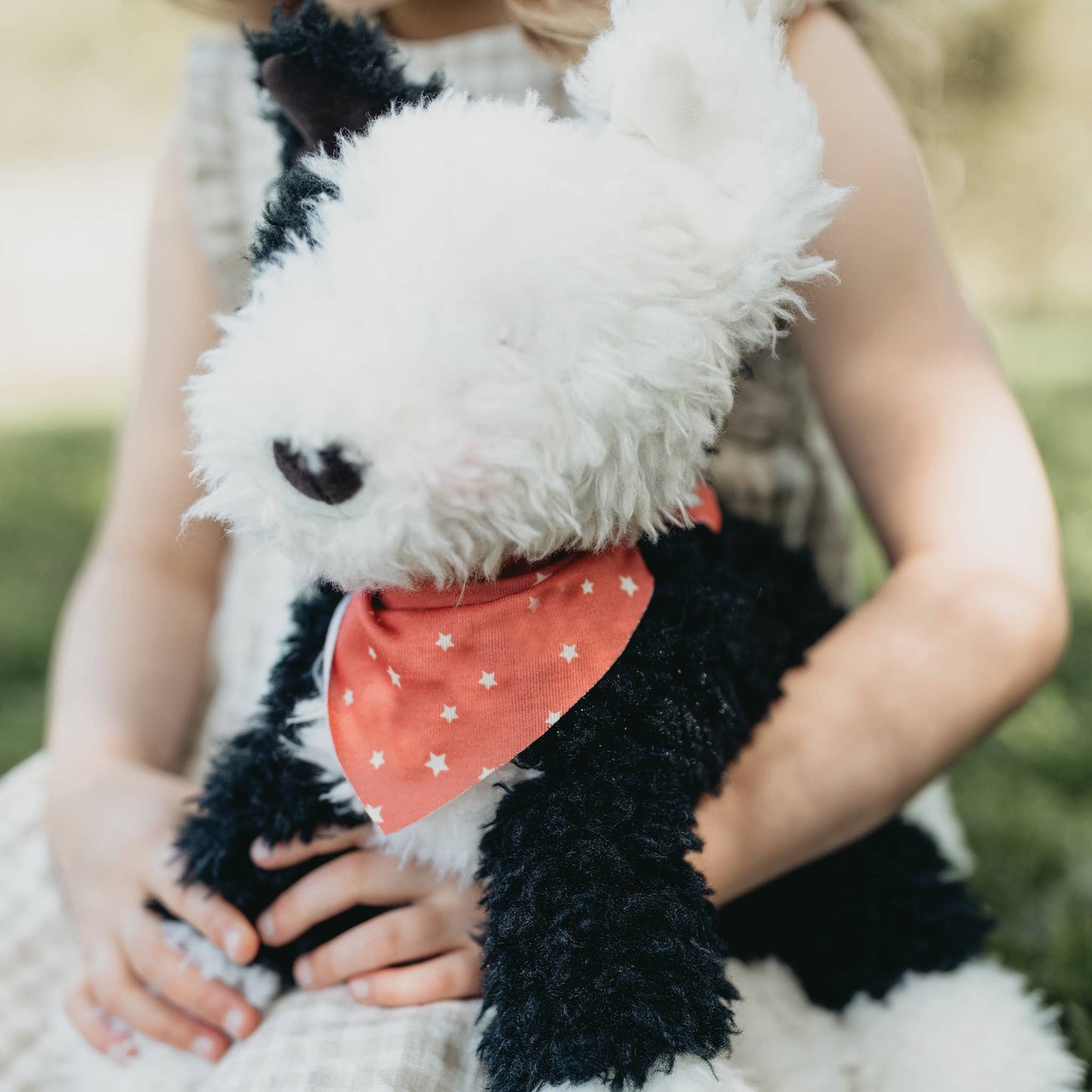 Person holding a plush dog toy with a red bandana outdoors