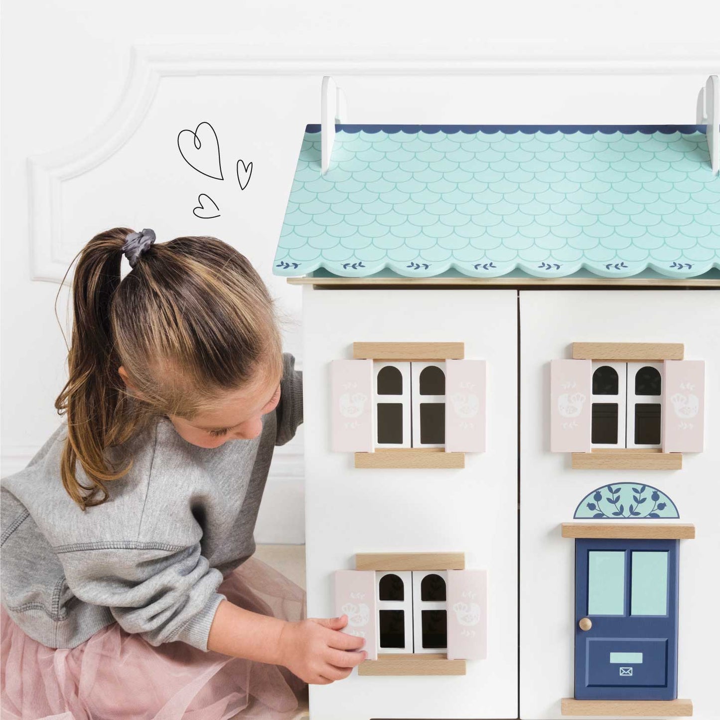 Child playing with a toy dollhouse with a blue roof and white walls.
