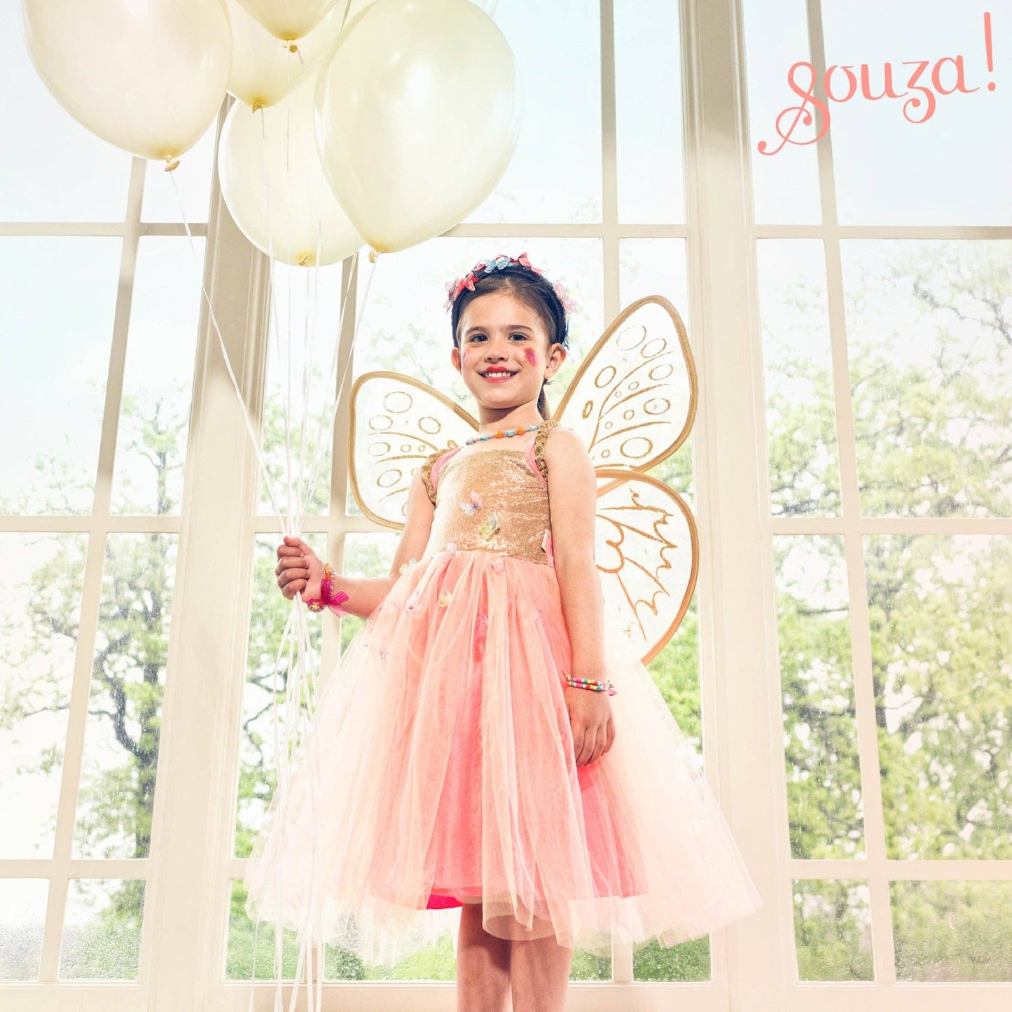 Young girl in a fairy costume with butterfly wings standing in front of a window with balloons.