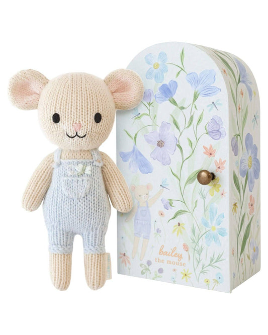 Knitted mouse toy with light blue overalls next to a floral-patterned box on a white background