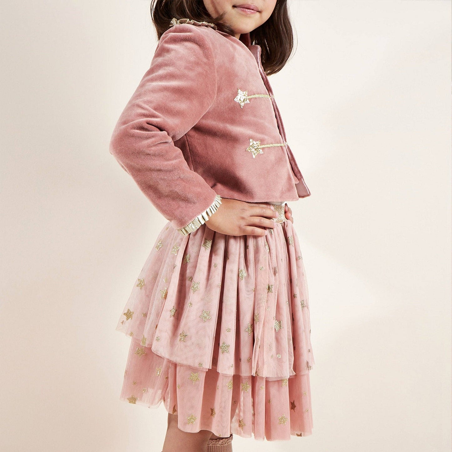Child wearing a pink outfit with a jacket and skirt on a plain background