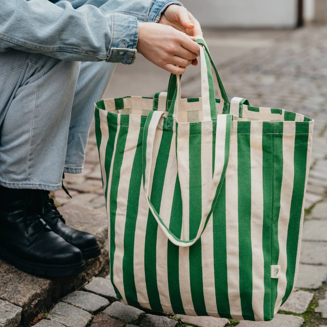 Person holding a green and white striped tote bag on a sidewalk.