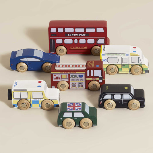 Set of wooden toy vehicles including a red bus, police car, fire truck, black taxi and others on a beige background.