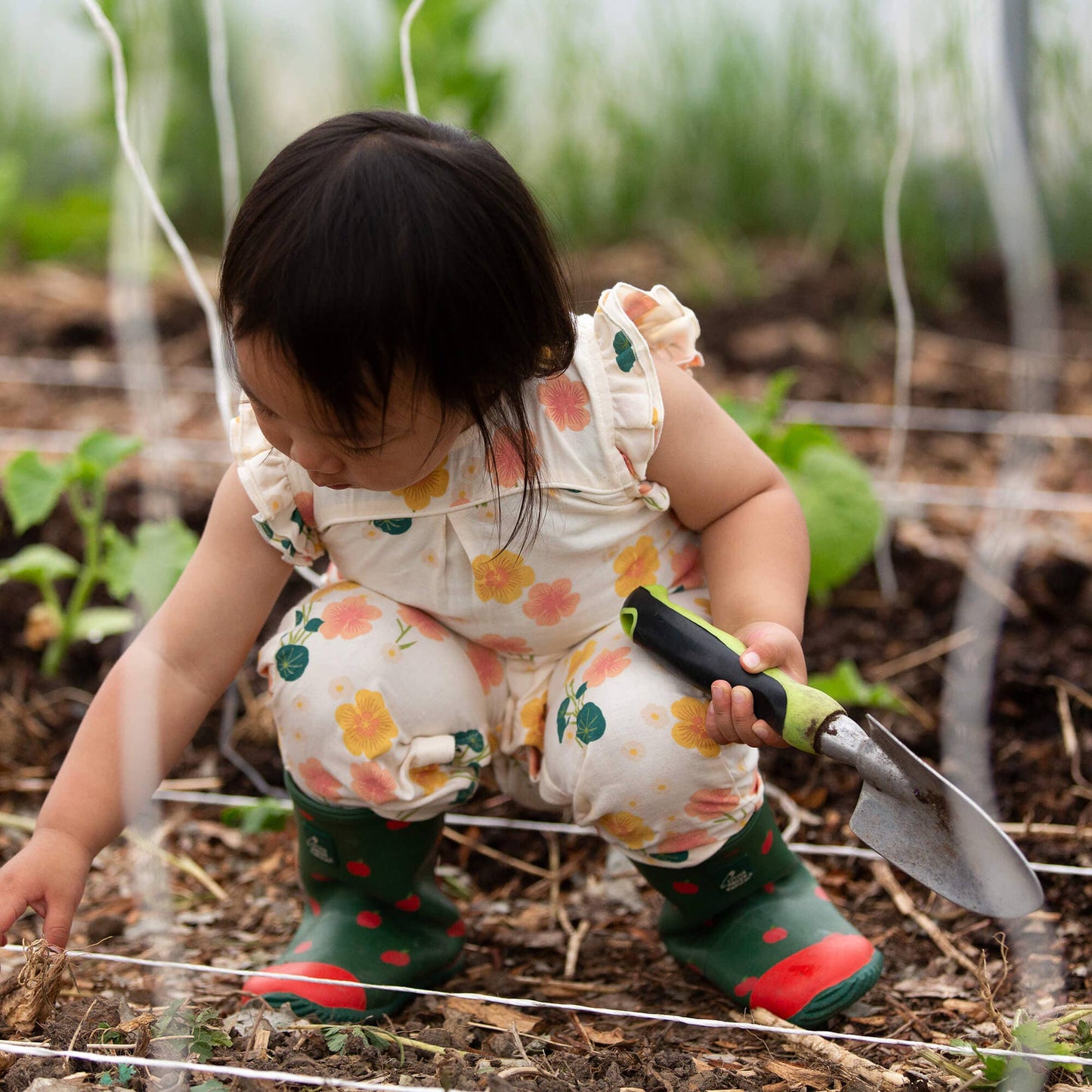 Child in a garden holding a small gardening tool