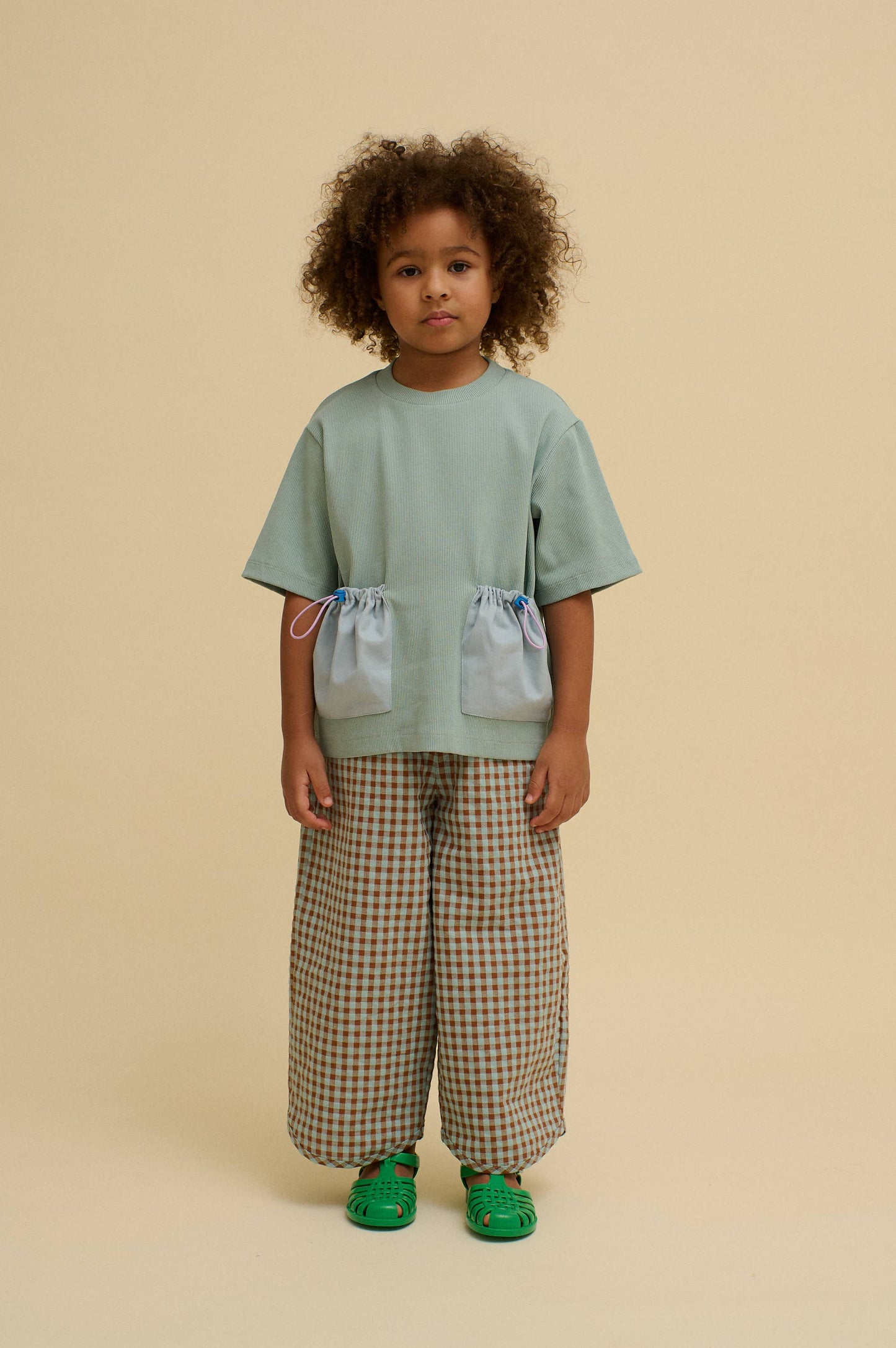 Child wearing a light green top and checkered pants on a beige background