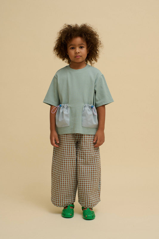 Child wearing a light green top and checkered pants on a beige background