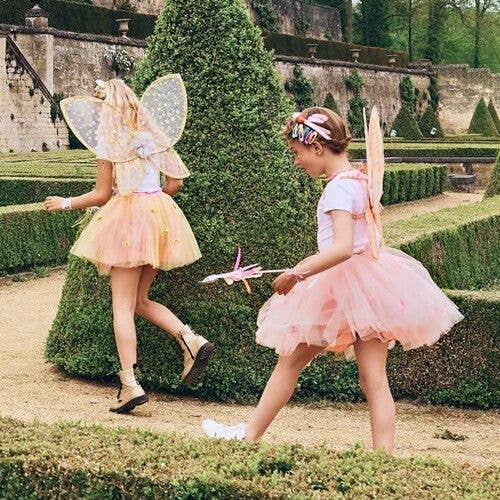 Two children in fairy costumes playing in a garden.