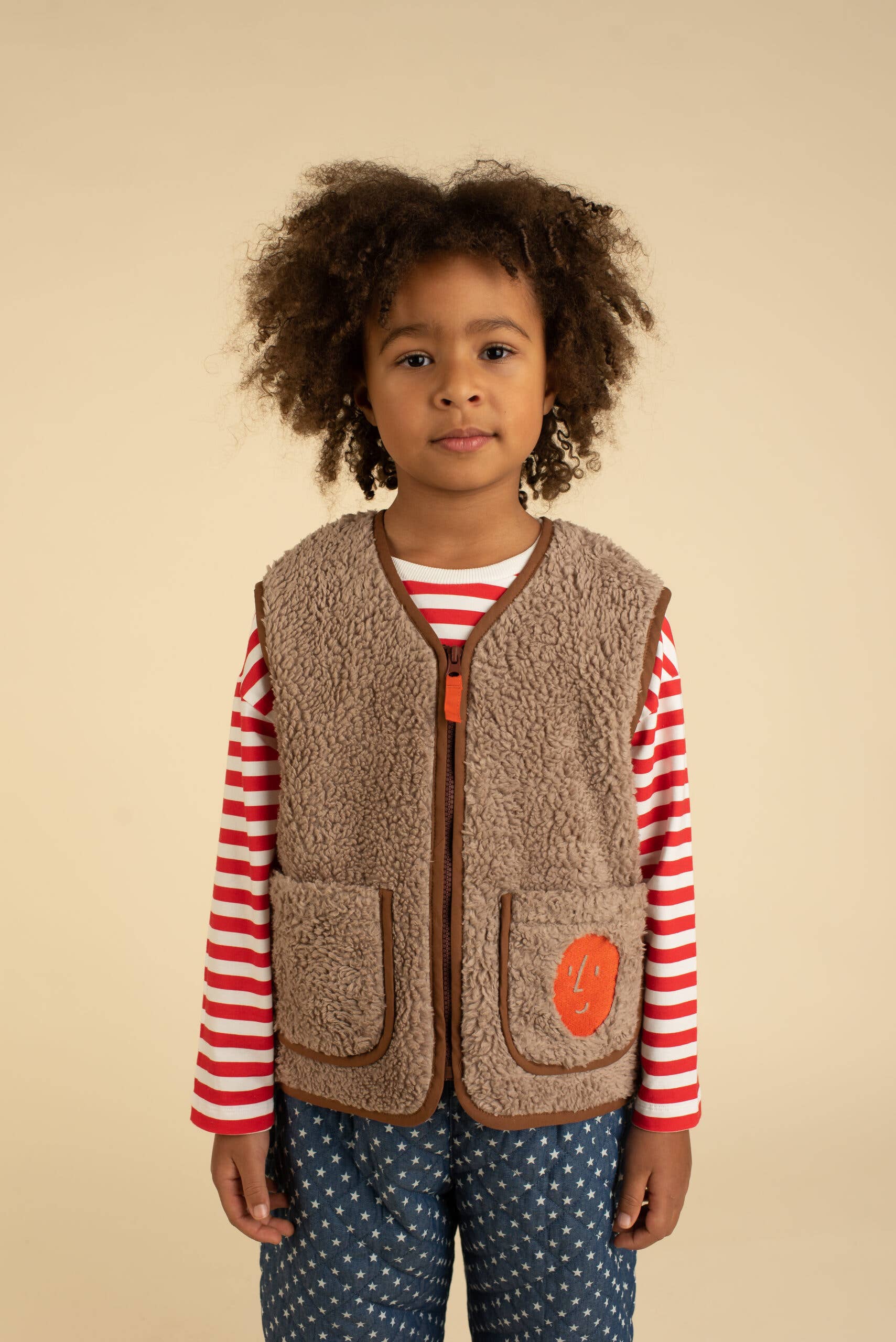 Child wearing a brown vest over a striped shirt with a beige background
