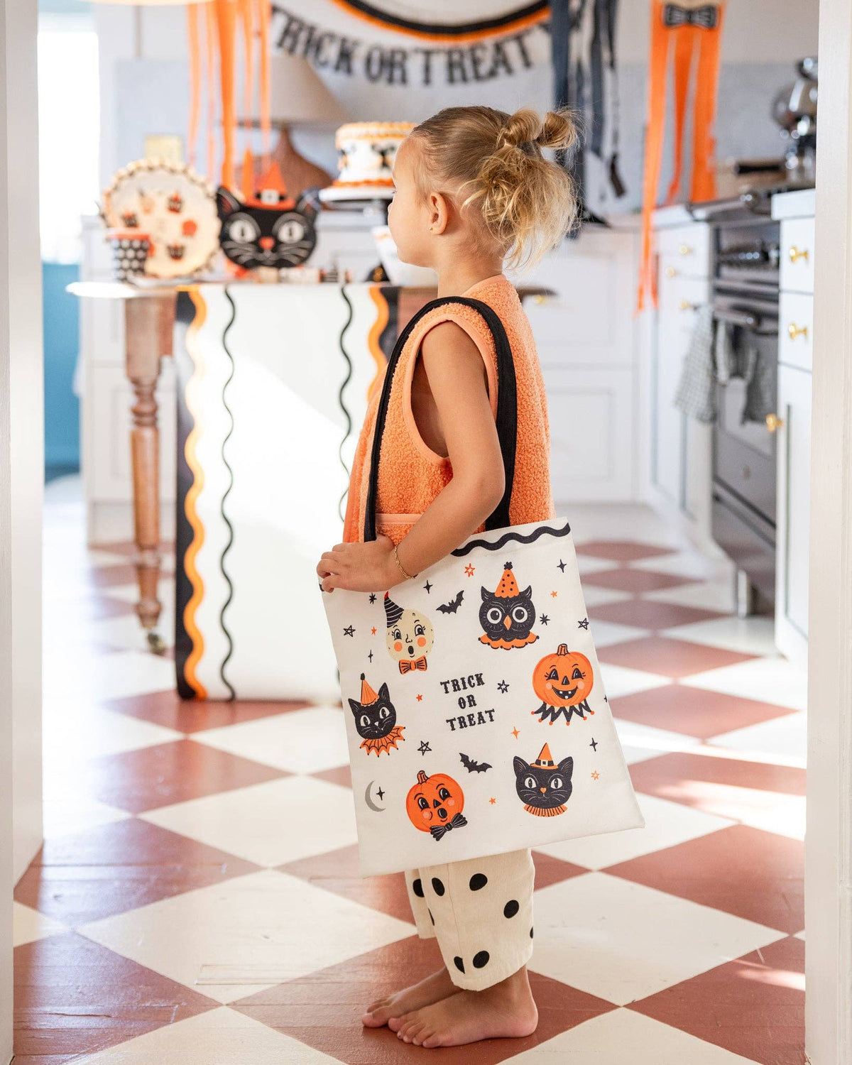 Child holding a Halloween-themed bag in a decorated kitchen
