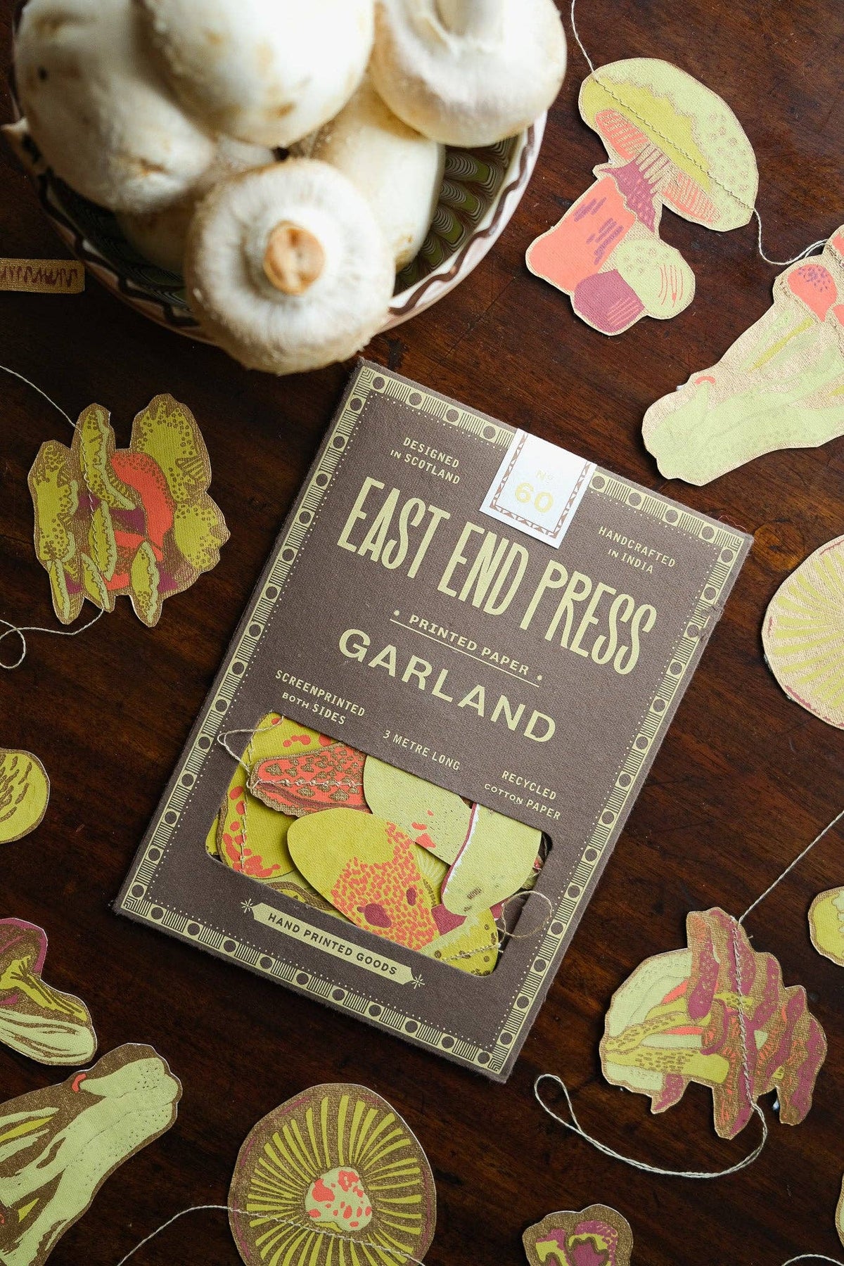 Mushroom garland and its East End Press packaging on dark wood beside a bowl of garlic.