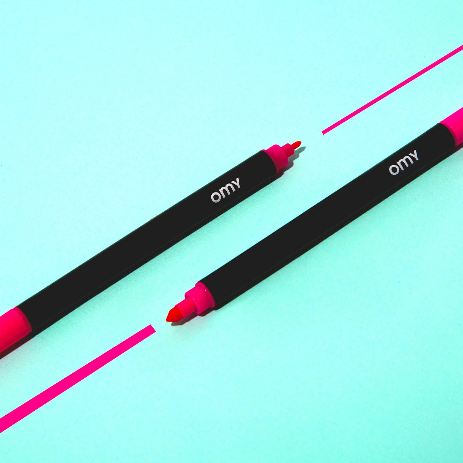 Two black markers with pink tips on a light blue background, featuring the brand 'omy'.