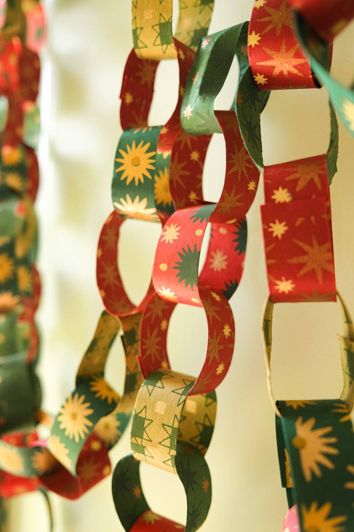 Close-up of hanging red, green and gold paper chains with sunburst and star patterns.