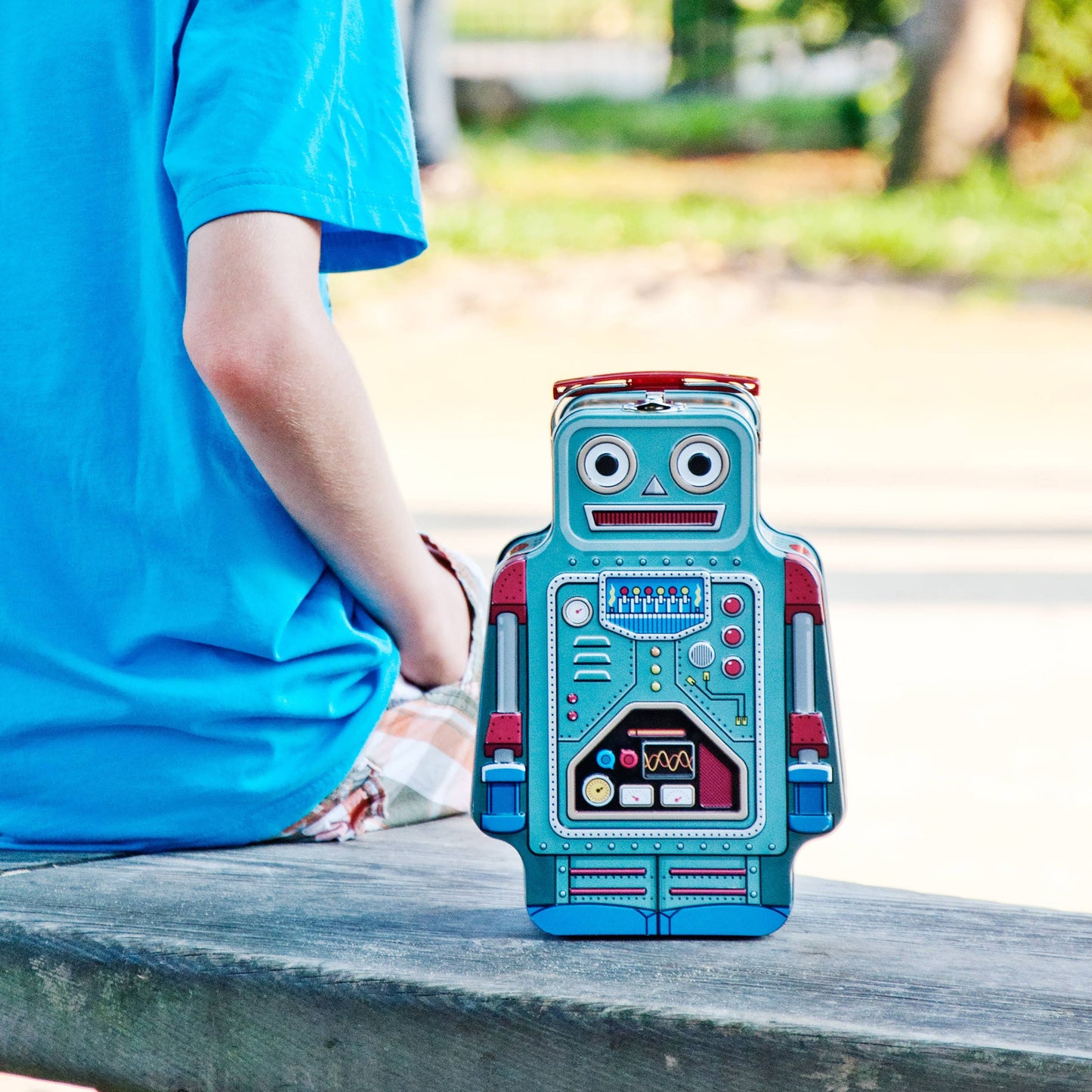 robot lunchbox on a bench with a child in a blue shirt sitting next to it