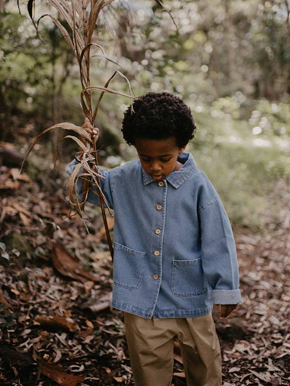 Child in a denim jacket holding a plant in a forest setting
