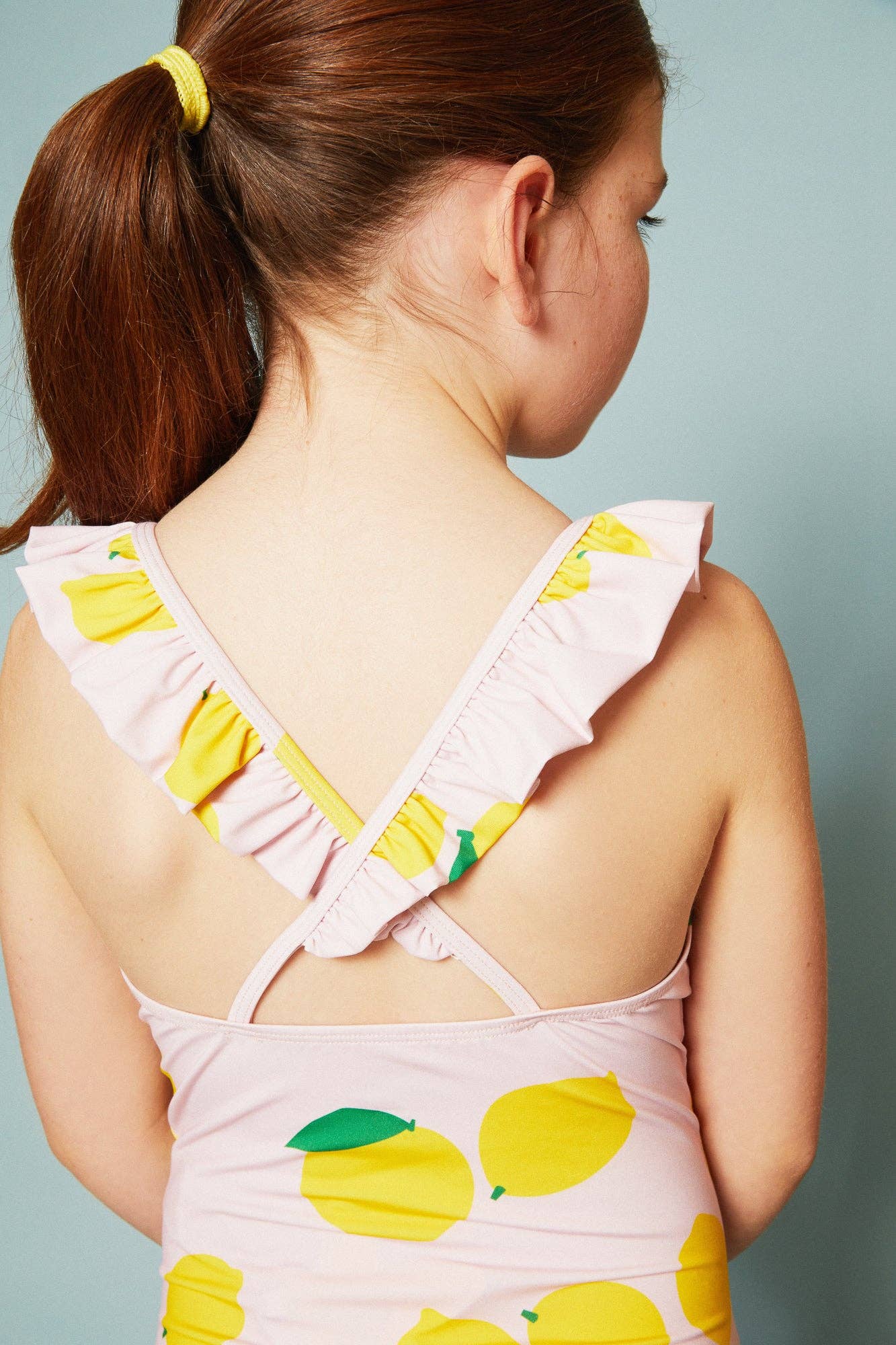 Back of child wearing a pink swimsuit with lemon print on a light blue background