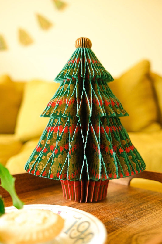 Green honeycomb fir tree decoration with red and gold patterns on a wooden tray in front of a yellow sofa.