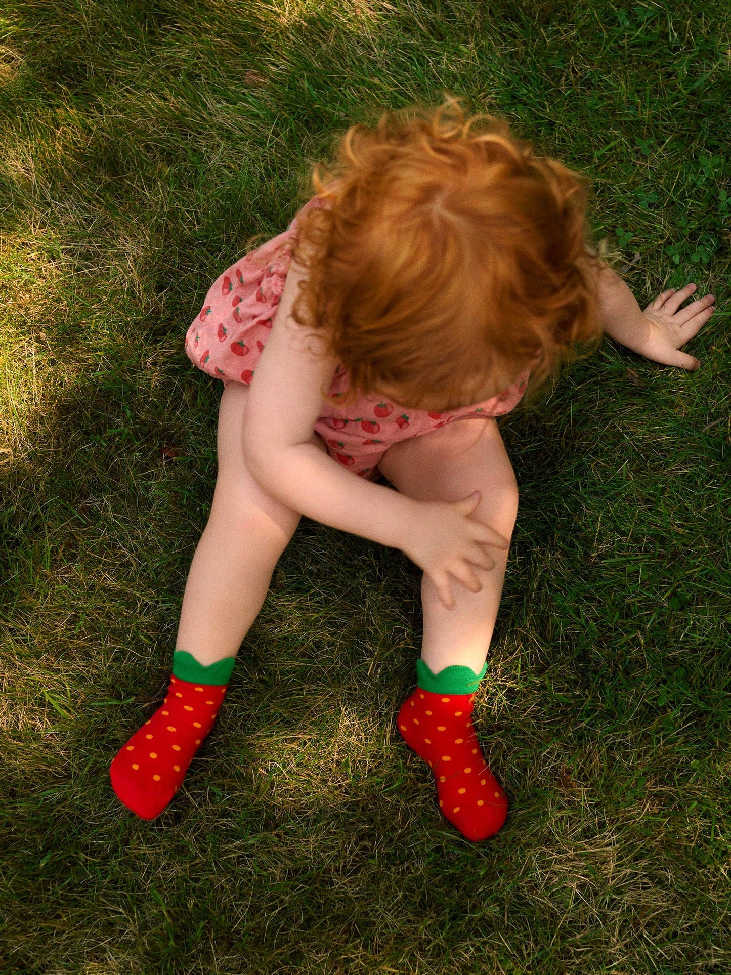 Child sitting on grass wearing red strawberry socks