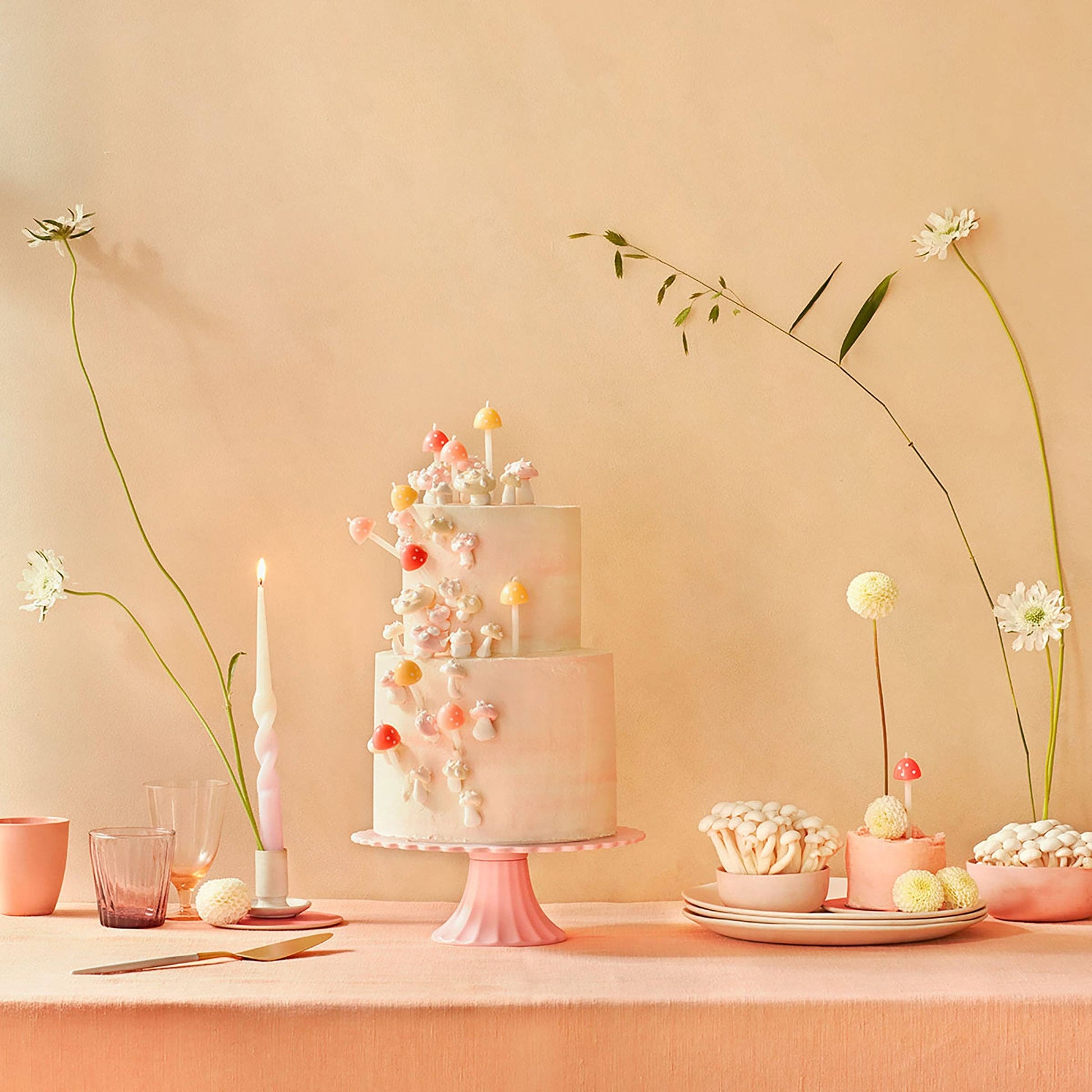 Three-tiered cake with decorative elements on a pink stand against a beige background
