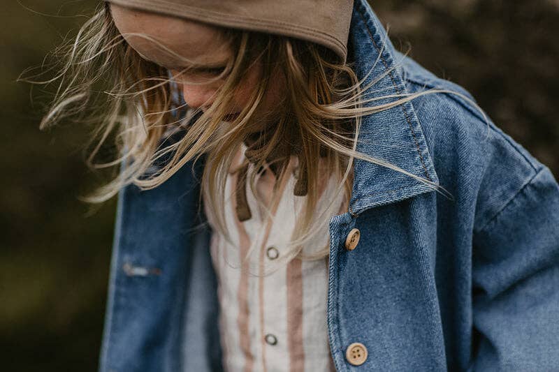 Child wearing a denim jacket and beige cap with a blurred background
