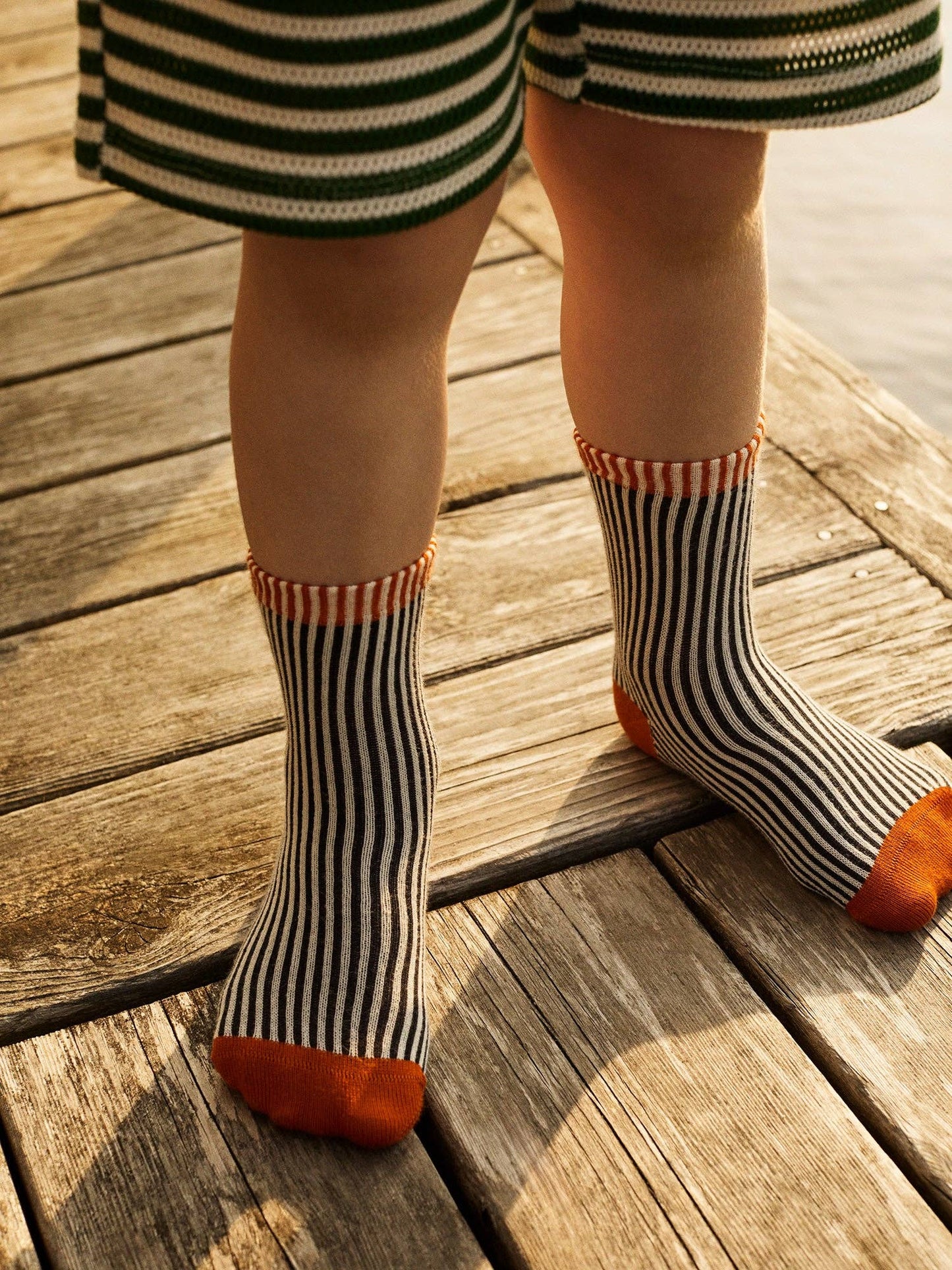 Child wearing striped socks with orange toes on a wooden floor