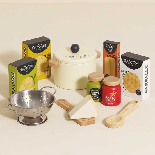 Set of toy kitchen items including a pot, colander, and boxes labeled 'Ravioli', 'Pesto', and 'Farealle' on a light background.
