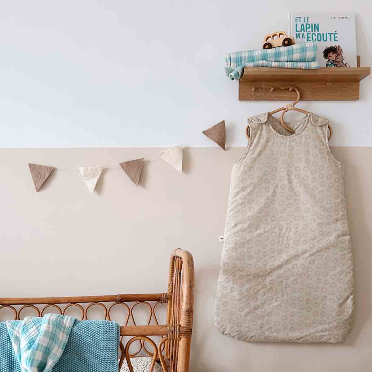Baby sleeping bag hanging on a hook with a wooden shelf and decorative elements in the background.