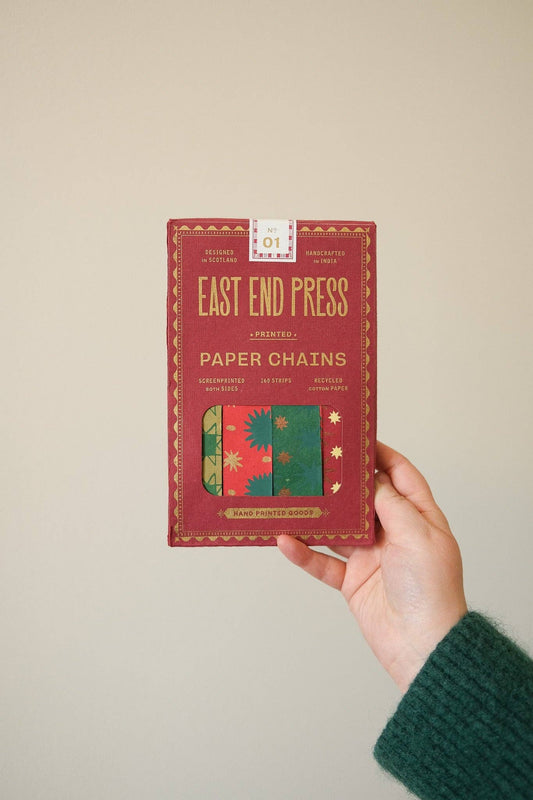 Hand holding the red East End Press Festive Paper Chain Kit box against a plain background.