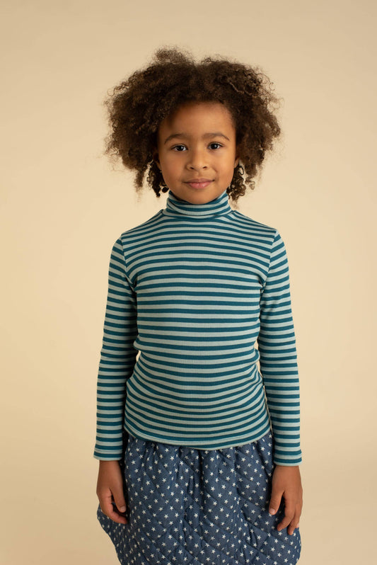Child wearing a green striped shirt with polka dot pants on a beige background