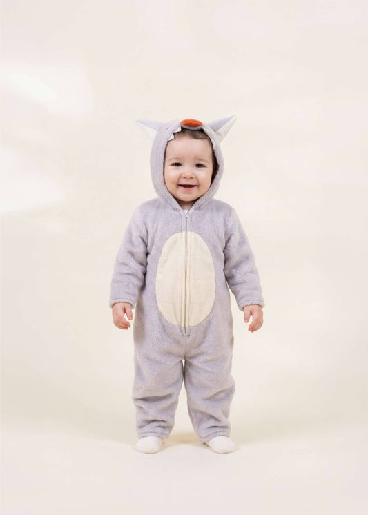 A baby wearing a light gray animal costume with a white belly patch, standing against a plain cream background.