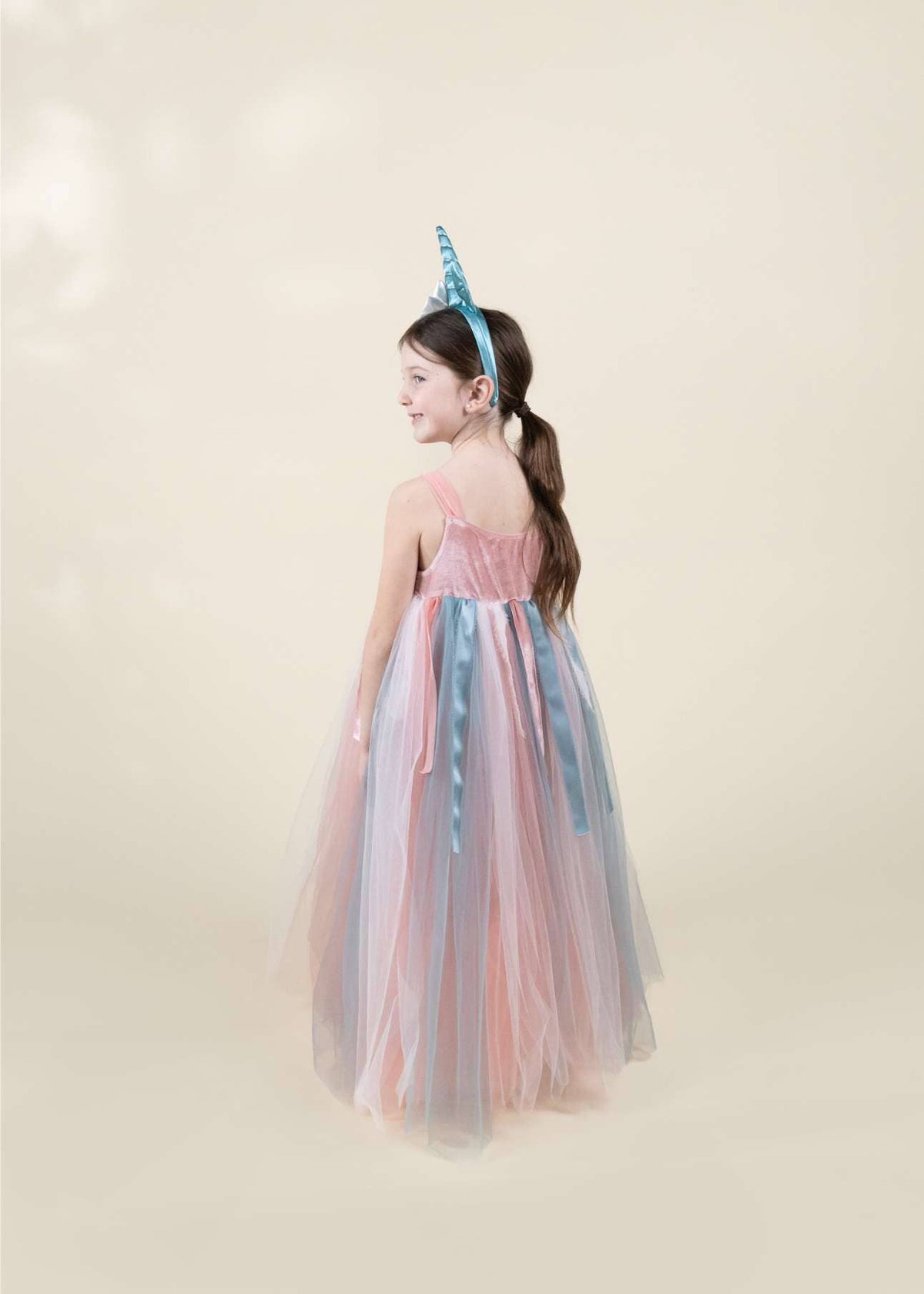 Young girl in a colorful dress with a unicorn horn headband on a plain background