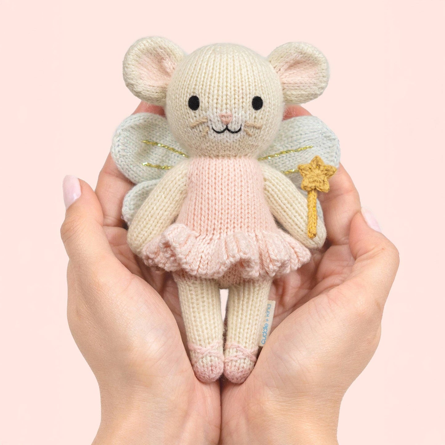 Knitted fairy mouse toy held in hands against a pink background