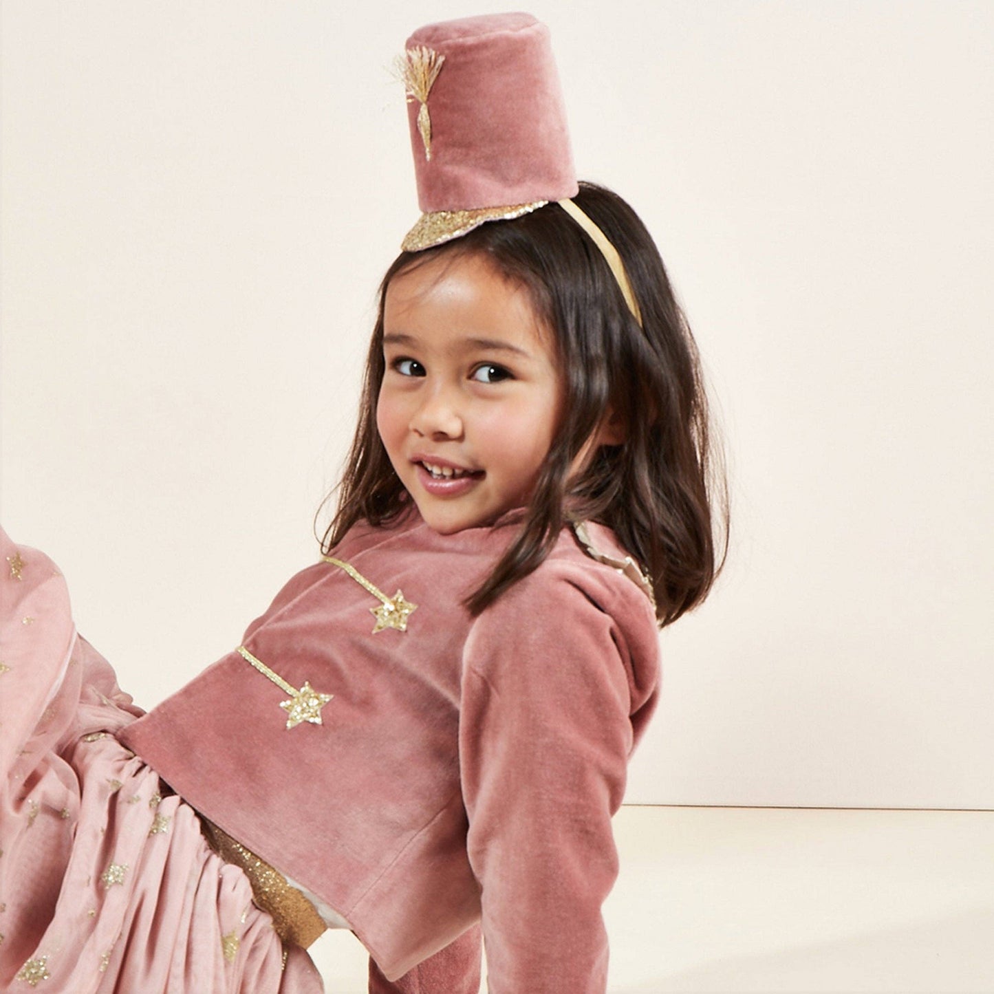 Young girl in a pink costume with a hat, sitting against a light background