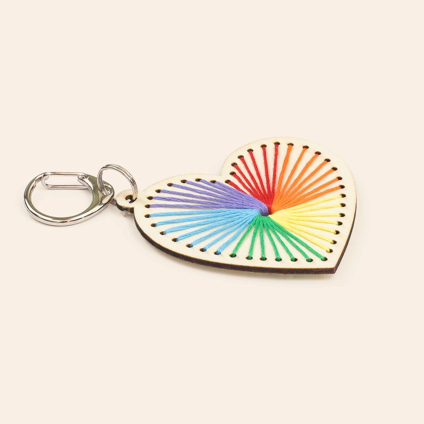 Wooden heart-shaped keychain with rainbow string design on a beige background