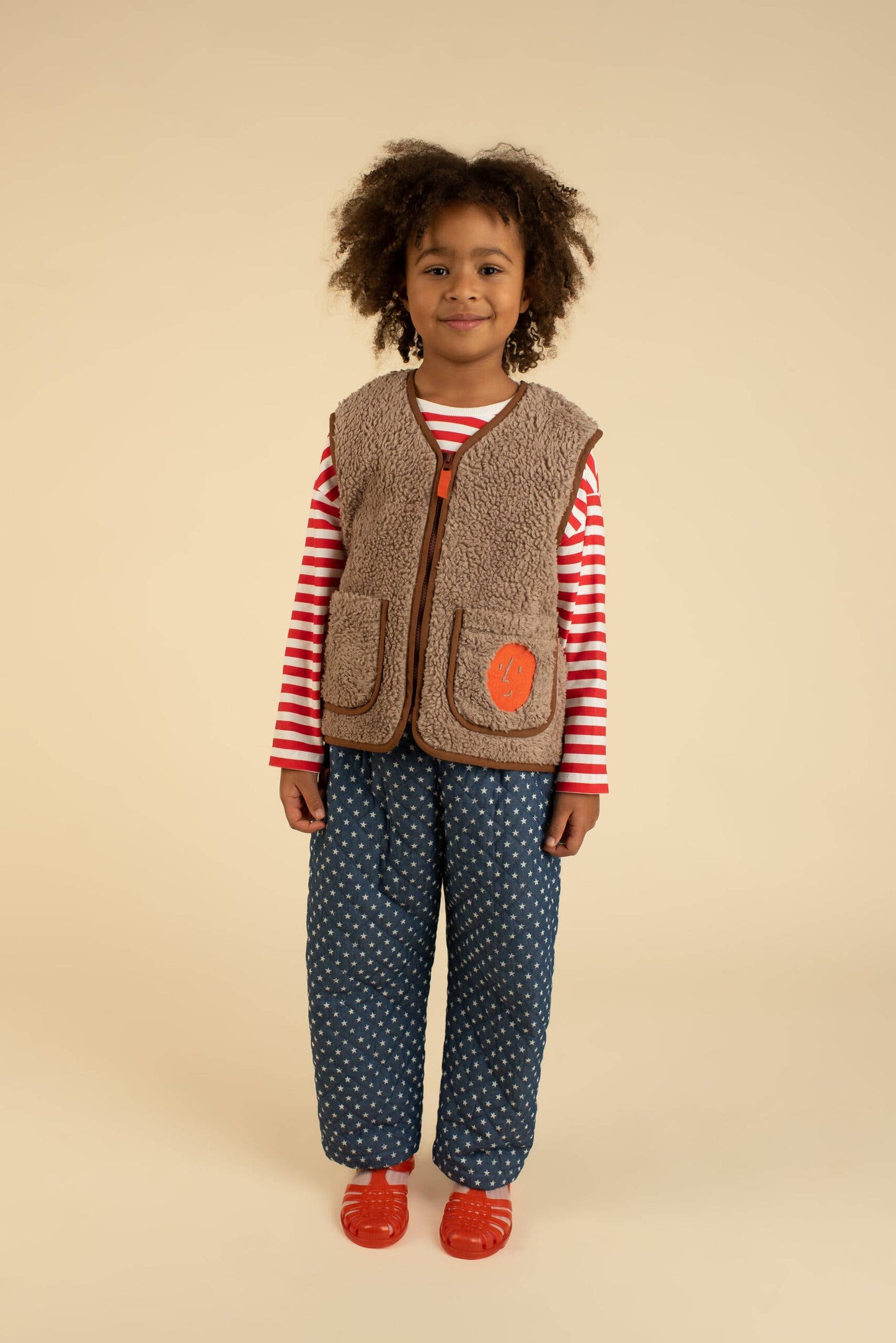 Child wearing a striped shirt, vest, and polka dot pants on a beige background
