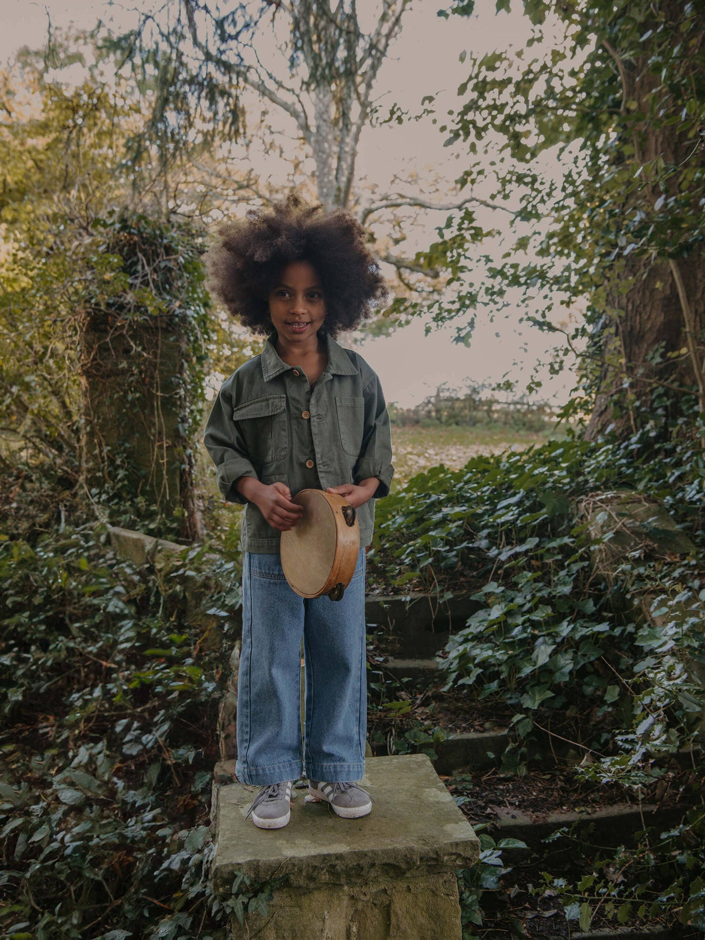 Child standing on a stone step in a garden with greenery in the background
