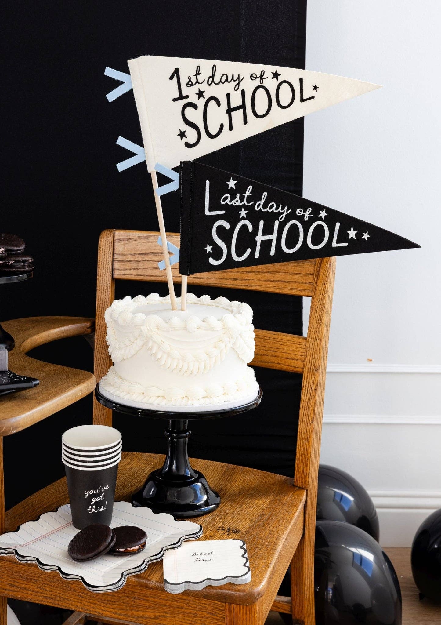White cake on a wooden chair with '1st Day of School' and 'Last Day of School' signs.