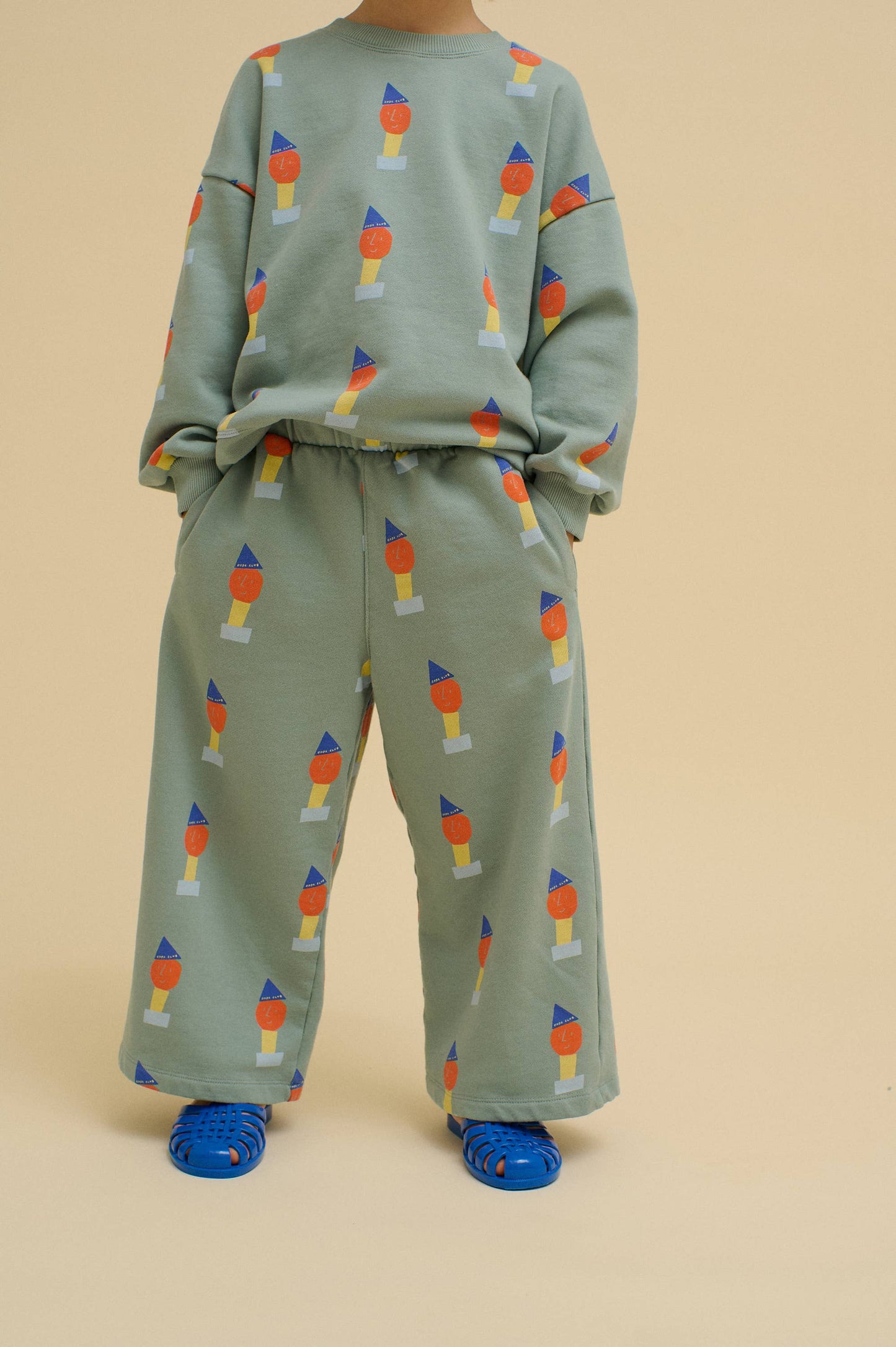Child wearing a green top and pant set with colorful pattern on a beige background