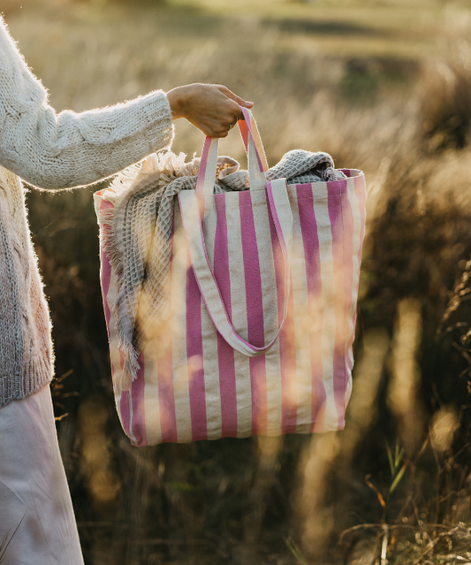 Person holding a pink and white striped tote bag with a blanket in a natural setting