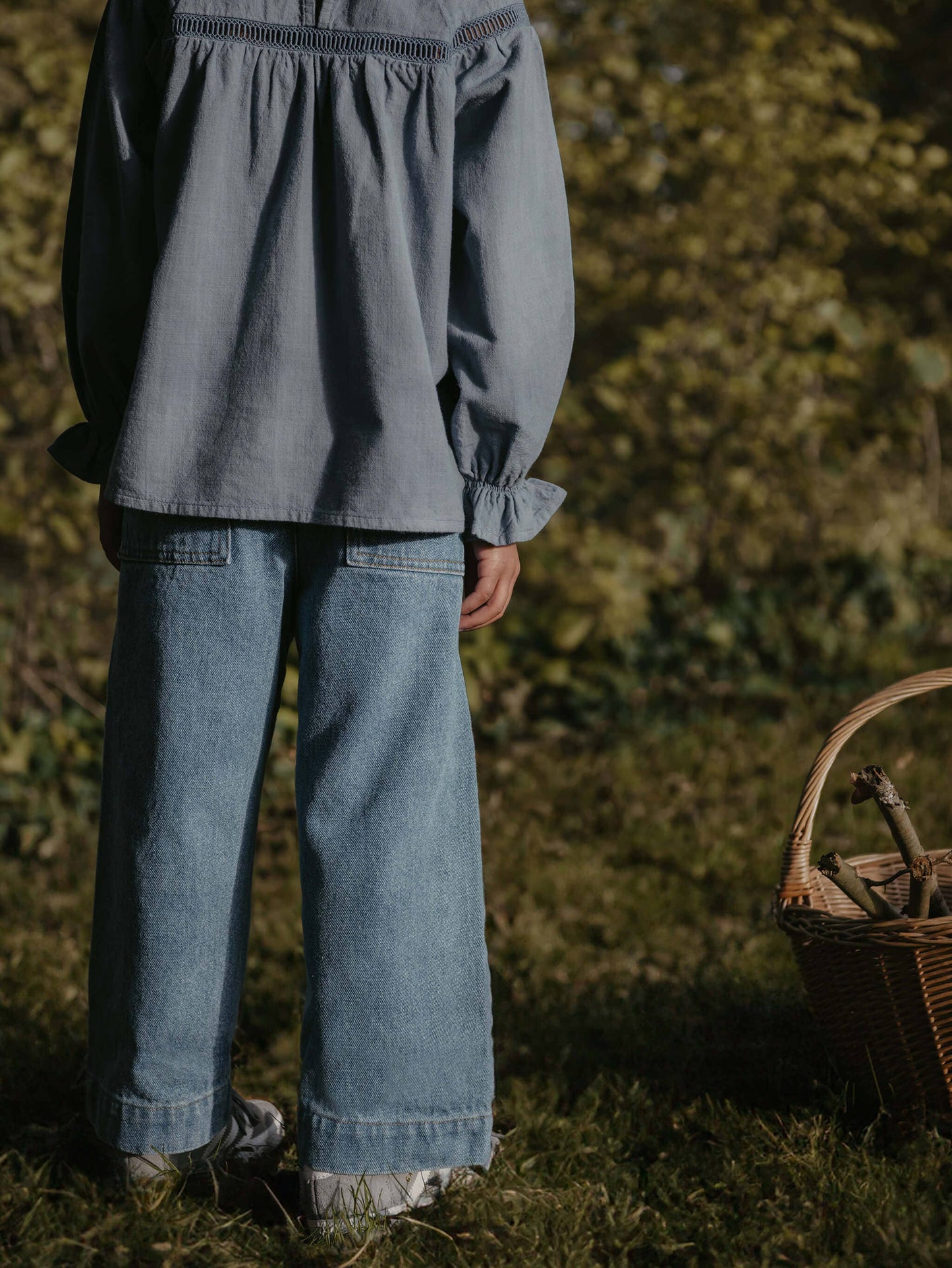 Child wearing a gray blouse and blue jeans standing outdoors with a basket in the foreground.