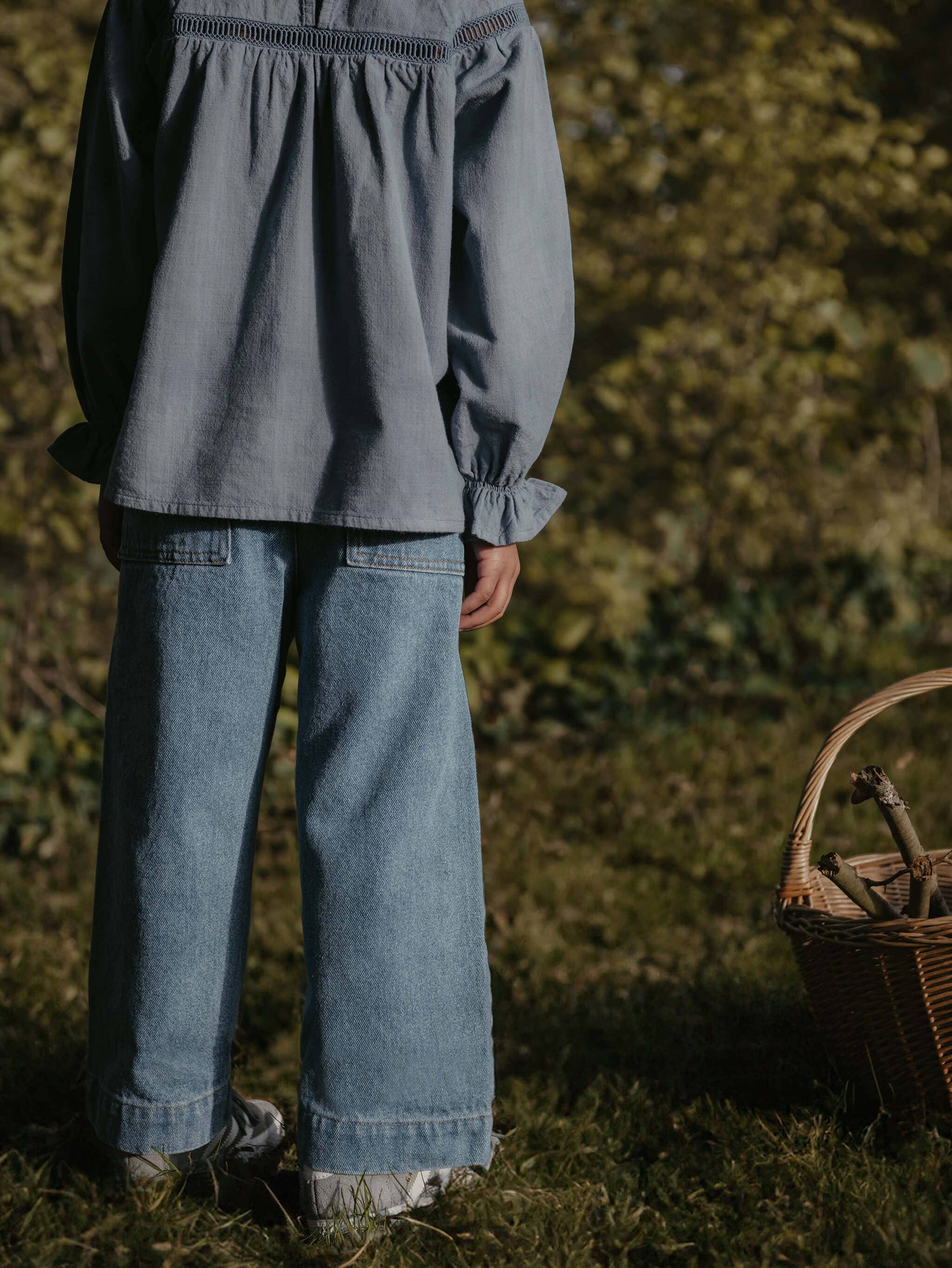 Child wearing a gray blouse and blue jeans standing outdoors with a basket in the foreground.