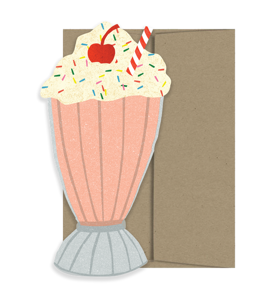 Cutout card with a design of a pink milkshake with whipped cream, a red cherry, and sprinkles on a brown background.