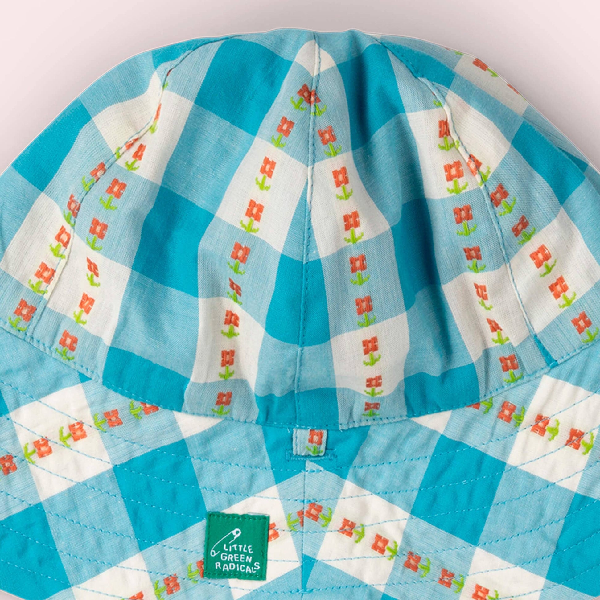 Close-up of a blue and white checkered fabric with floral patterns, featuring a brand label.
